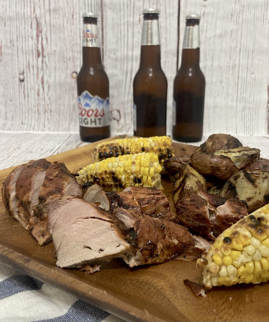summer grilling dinners, a cold beer with grilled corn, red skin potatoes and pork tenderloin on a wooden plate