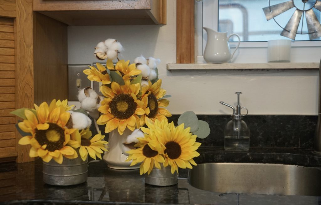 yellow sunflowers in measuring cups next to kitchen sink
