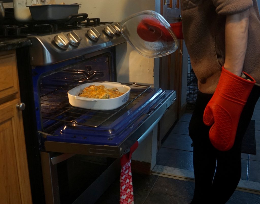woman taking chicken casserole out of the oven