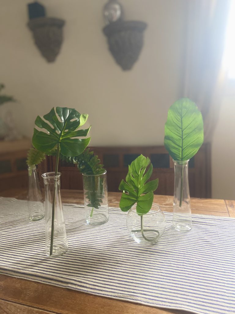 ferns and palms in glass jars on a blue and white stripe table runner