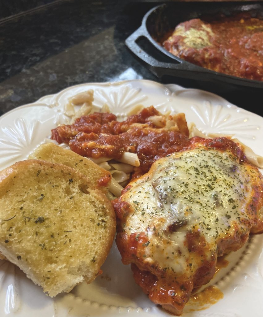 chicken parmesan on a white plate with garlic bread