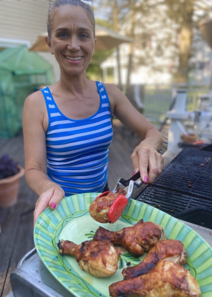 woman placing grilled chicken drumsticks on a platter