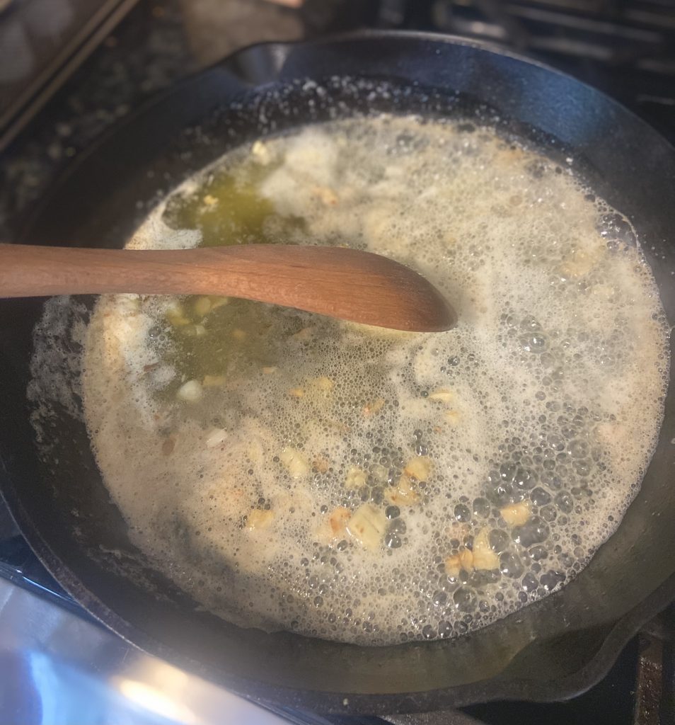 adding chopped garlic to a butter mixture in a cast iron skillet