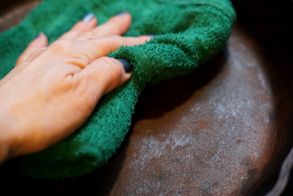 cleaning a cast iron skillet with a green cloth