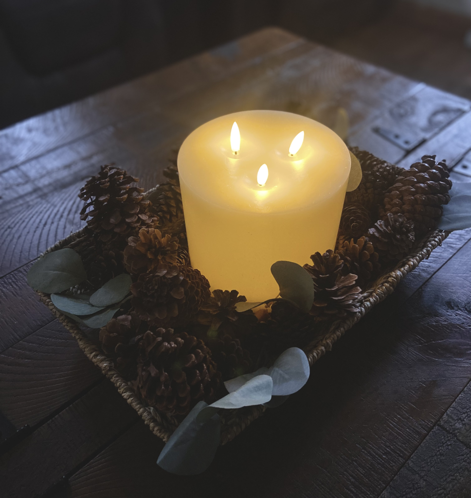 battery operated candle in a woven tray of pine and eucalyptus.