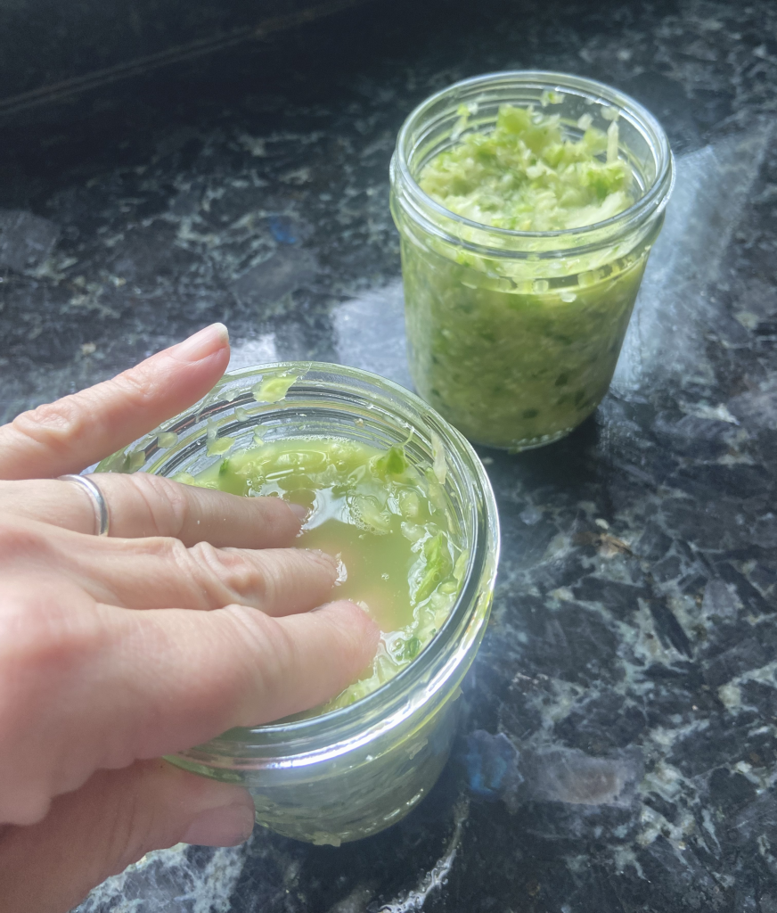 packing green lettuce in a glass mason jar to make sauerkraut