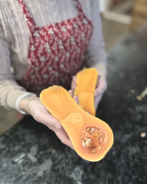 a woman in a apron cutting a butternut squash cut in half