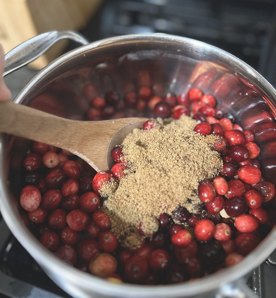 mixing in coconut sugar into Cranberry Sauce with a wooden spoon