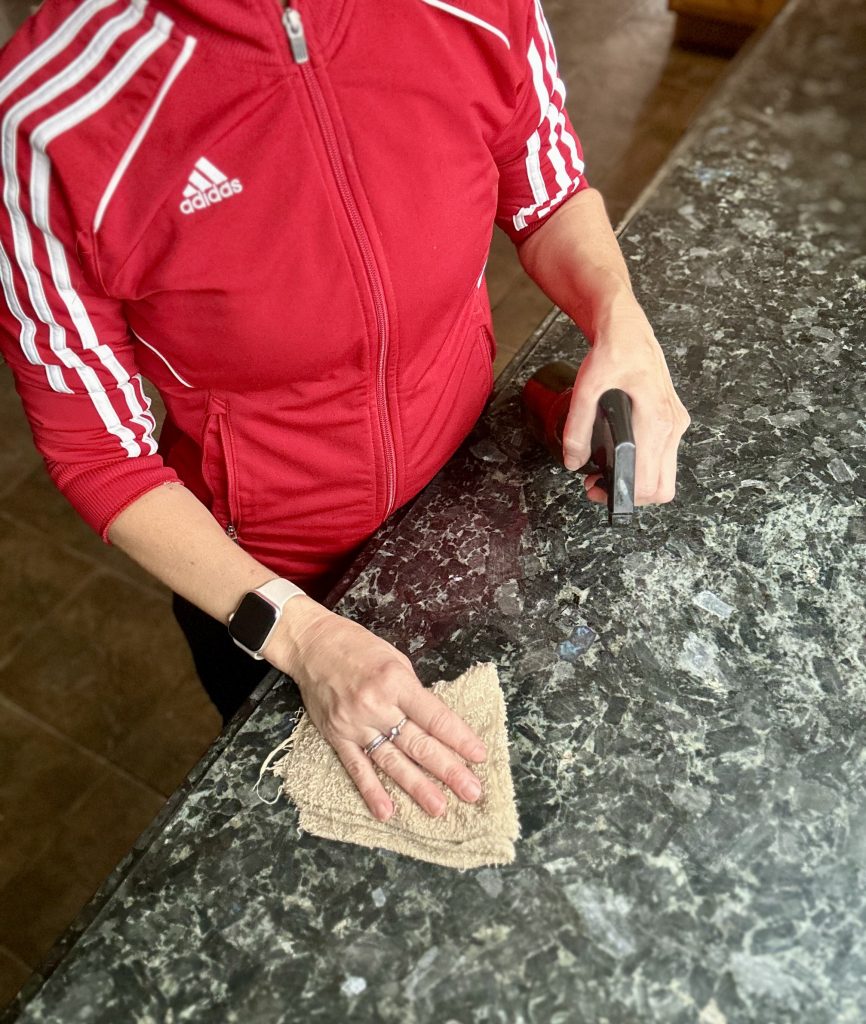 woman in a Red jacket cleaning counters with  Homemade Granite Cleaner