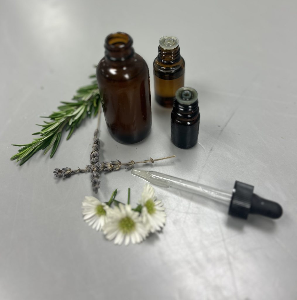 essential oil bottles, dropper and a spring of rosemary, lavender and white flowers